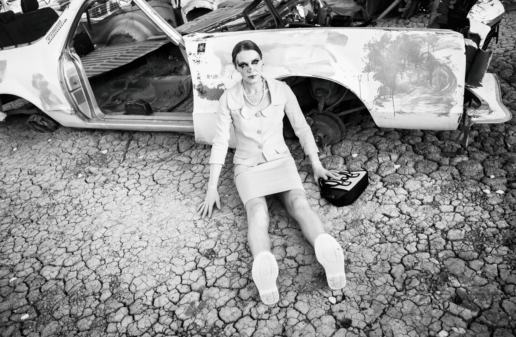 Discarded Ideals — A seated figure and a stripped car share the cracked ground. Photograph by Albert Pocej, California.