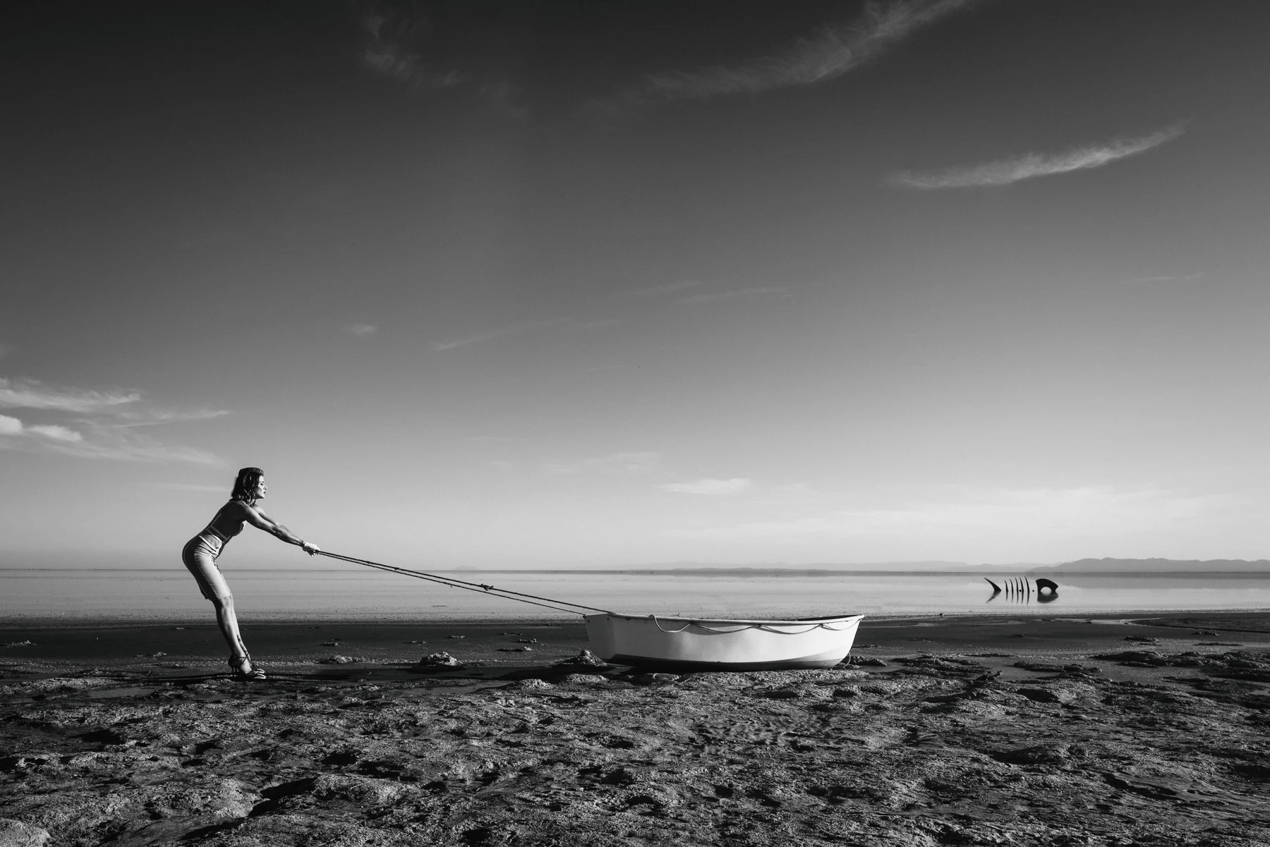 Echoes Of Rain — A small boat is pulled along the shore, opposite a fish-shaped structure. Photograph by Albert Pocej, California.