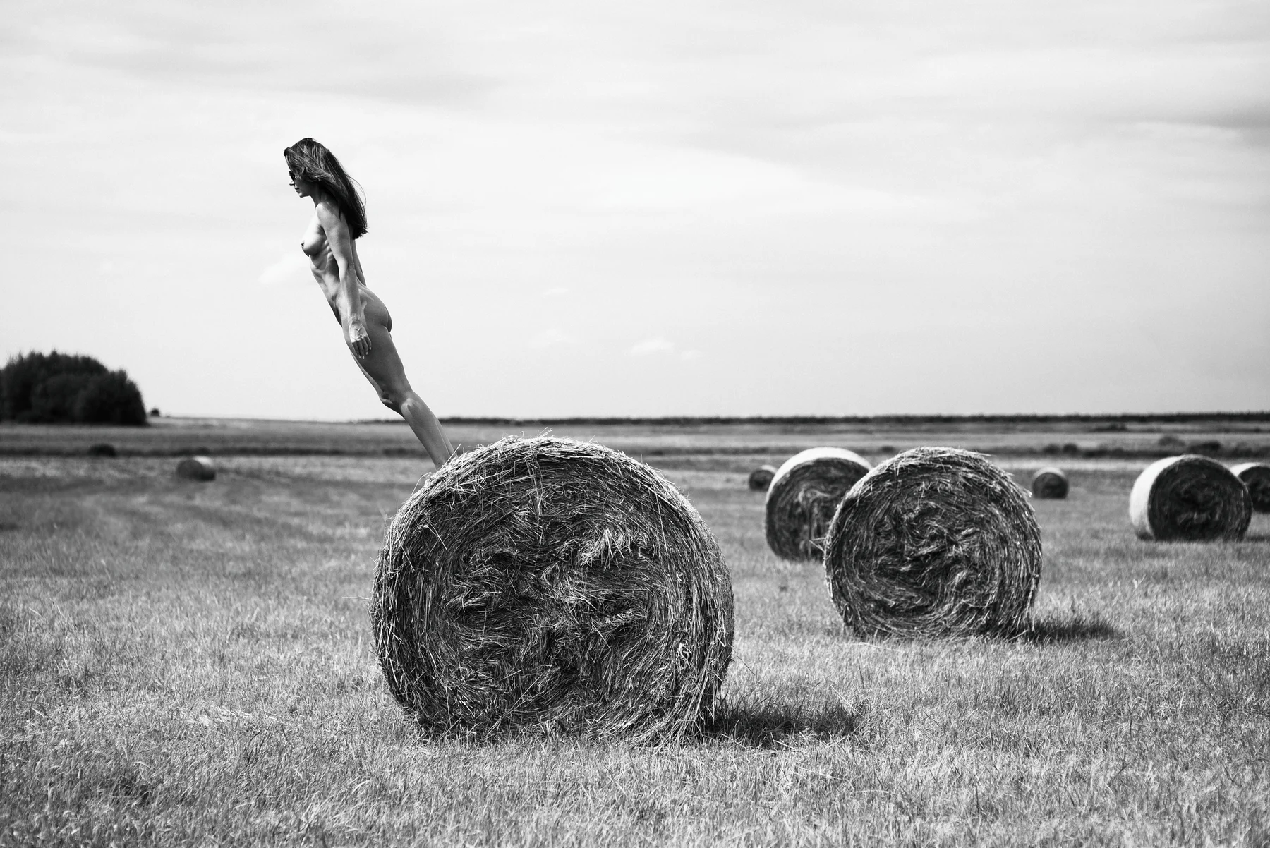 Field Of Gold — A body tips into the sky above a round hay bale. Photograph by Albert Pocej, Perfectly Normal.
