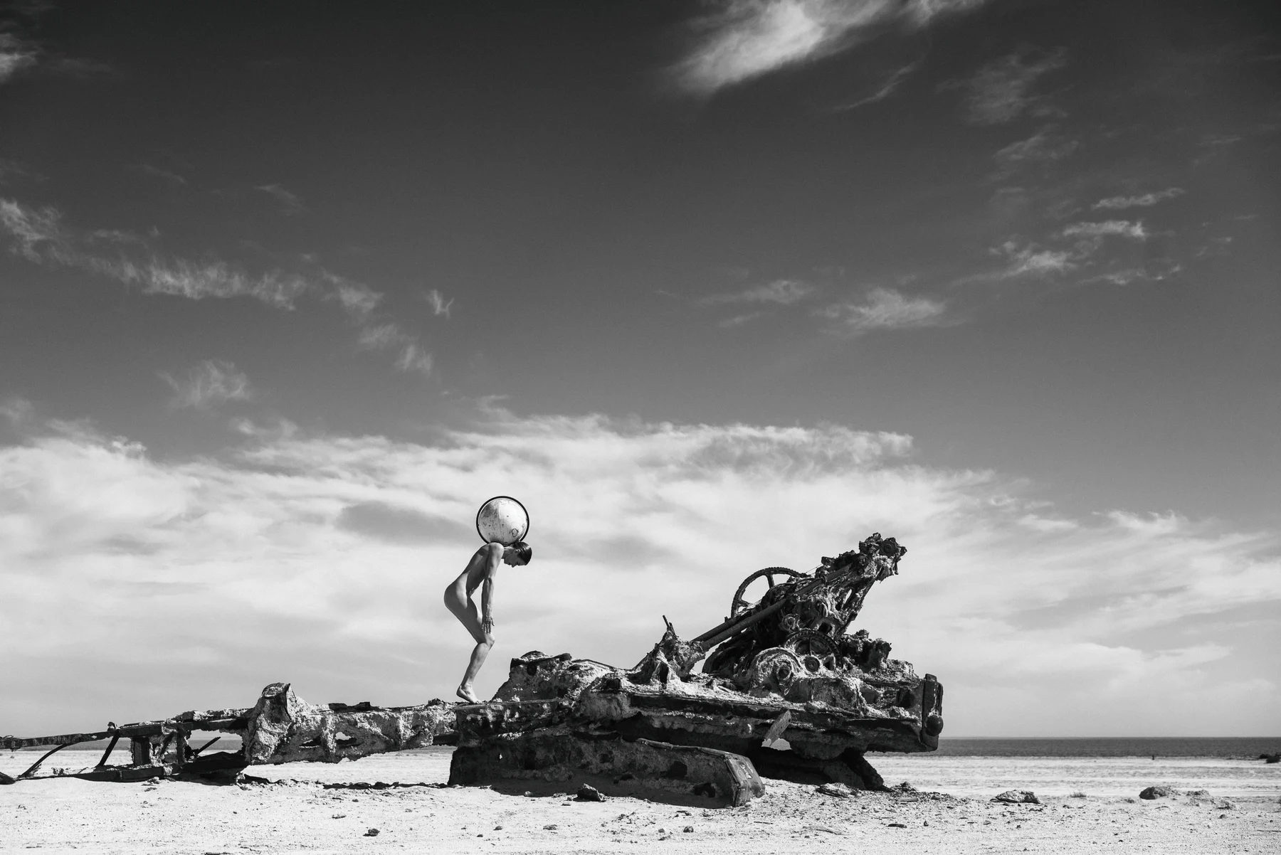 Global Pressure — A figure bends beneath a globe beside the remains of machinery. Photograph by Albert Pocej, California.