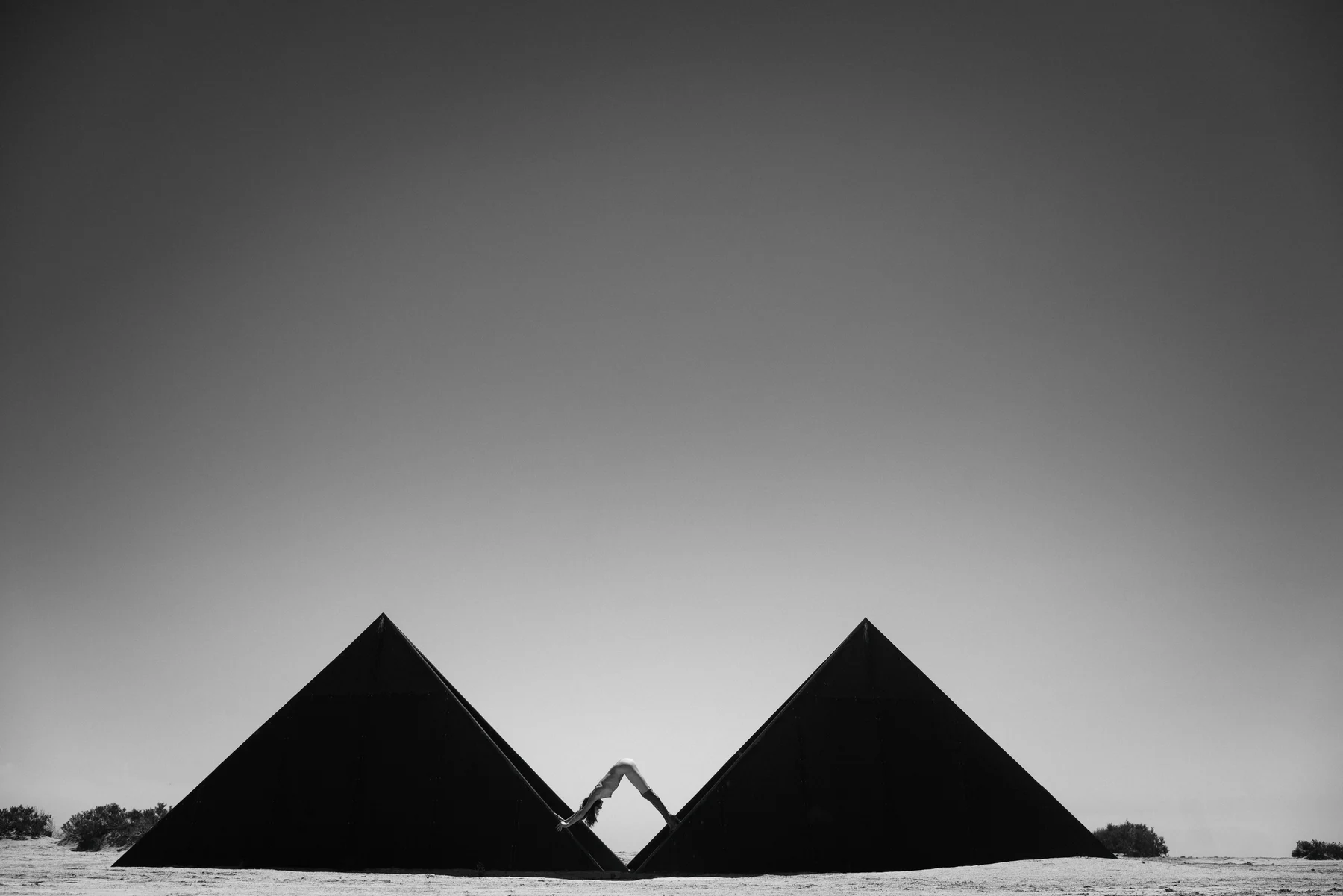 Mind The Gap — A body completes the geometry between two dark triangular structures. Photograph by Albert Pocej, California.