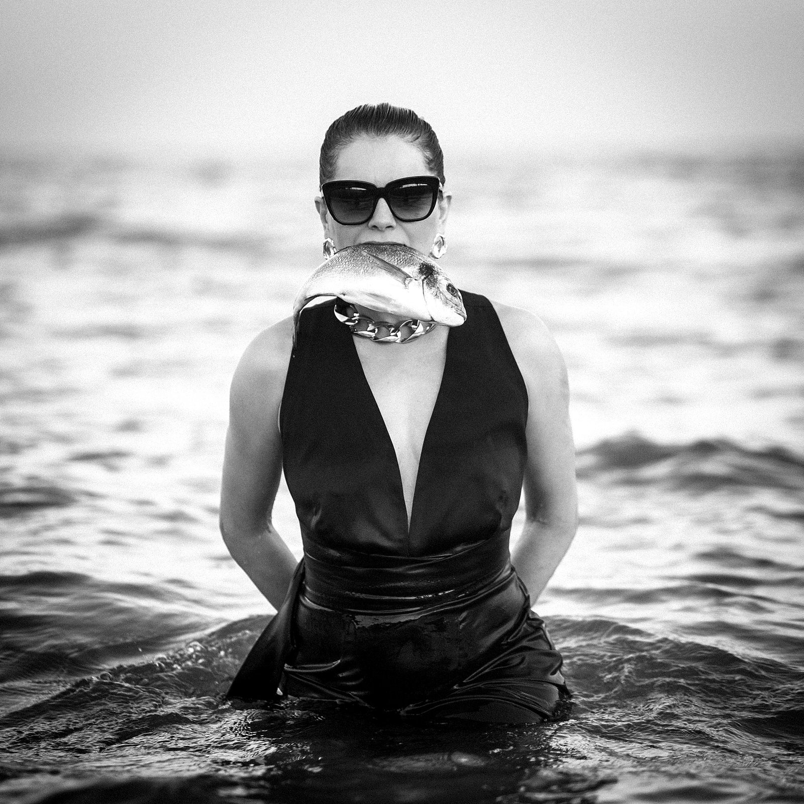 Silk And Salt — A fish held across the mouth; an evening dress in the water. Photograph by Albert Pocej, On the Edge.