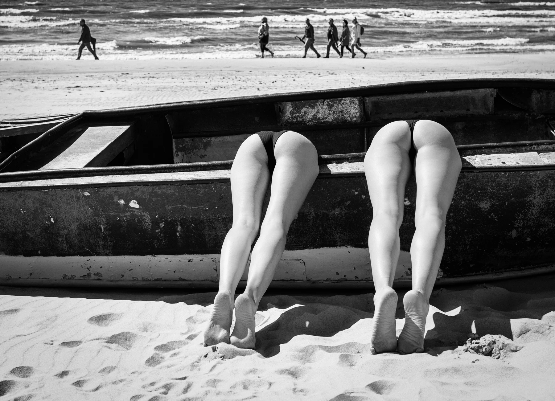 Sunbathers Anonymous — Two pairs of legs emerge from a boat on a busy beach. Photograph by Albert Pocej, Attachment Issues.