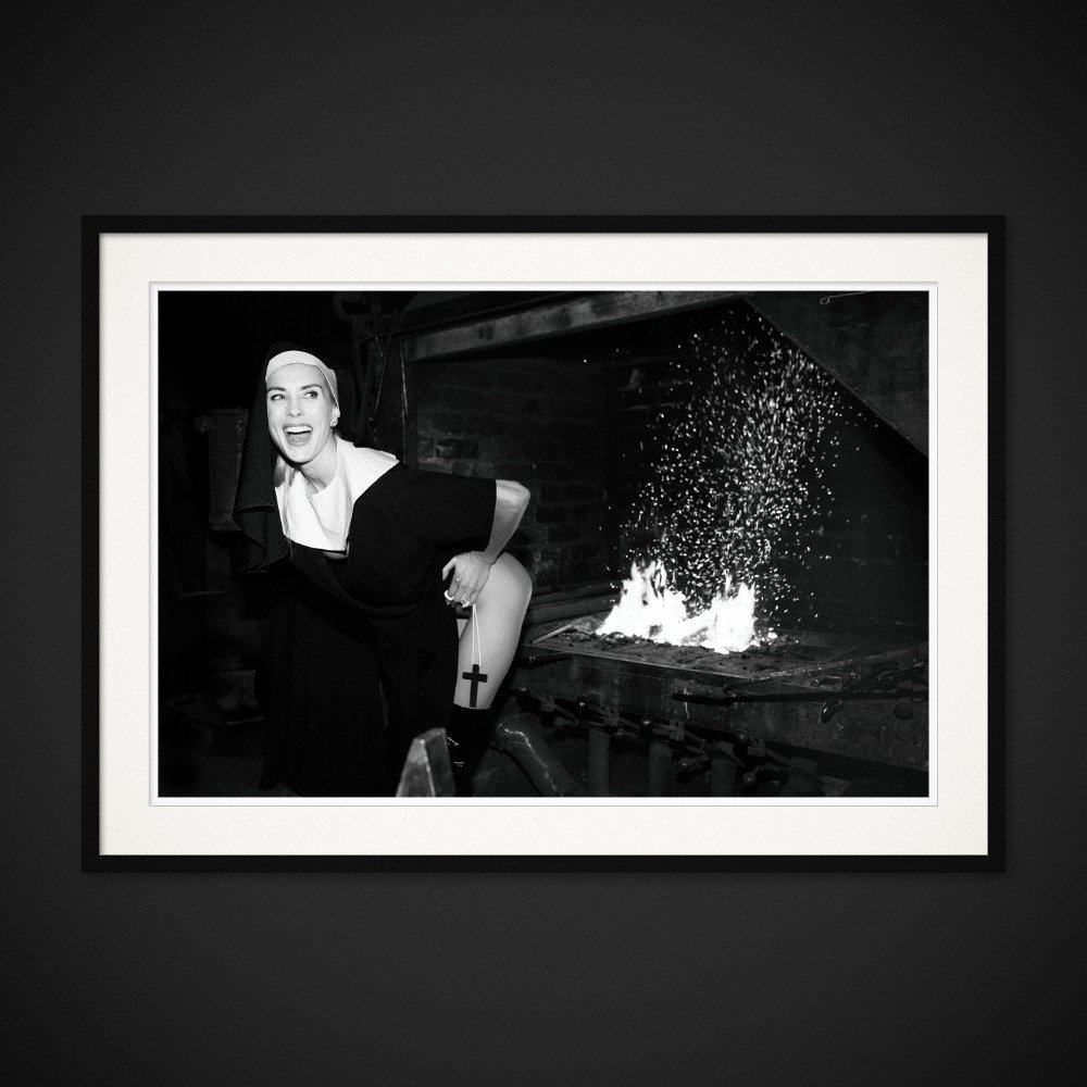 Confession — A nun’s habit, a raised hem and a smile beside the fire. Framed edition by Albert Pocej.