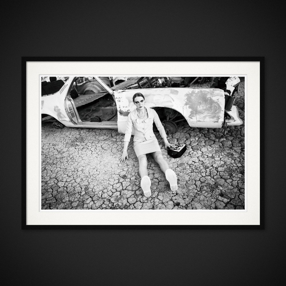 Discarded Ideals — A seated figure and a stripped car share the cracked ground. Framed edition by Albert Pocej.