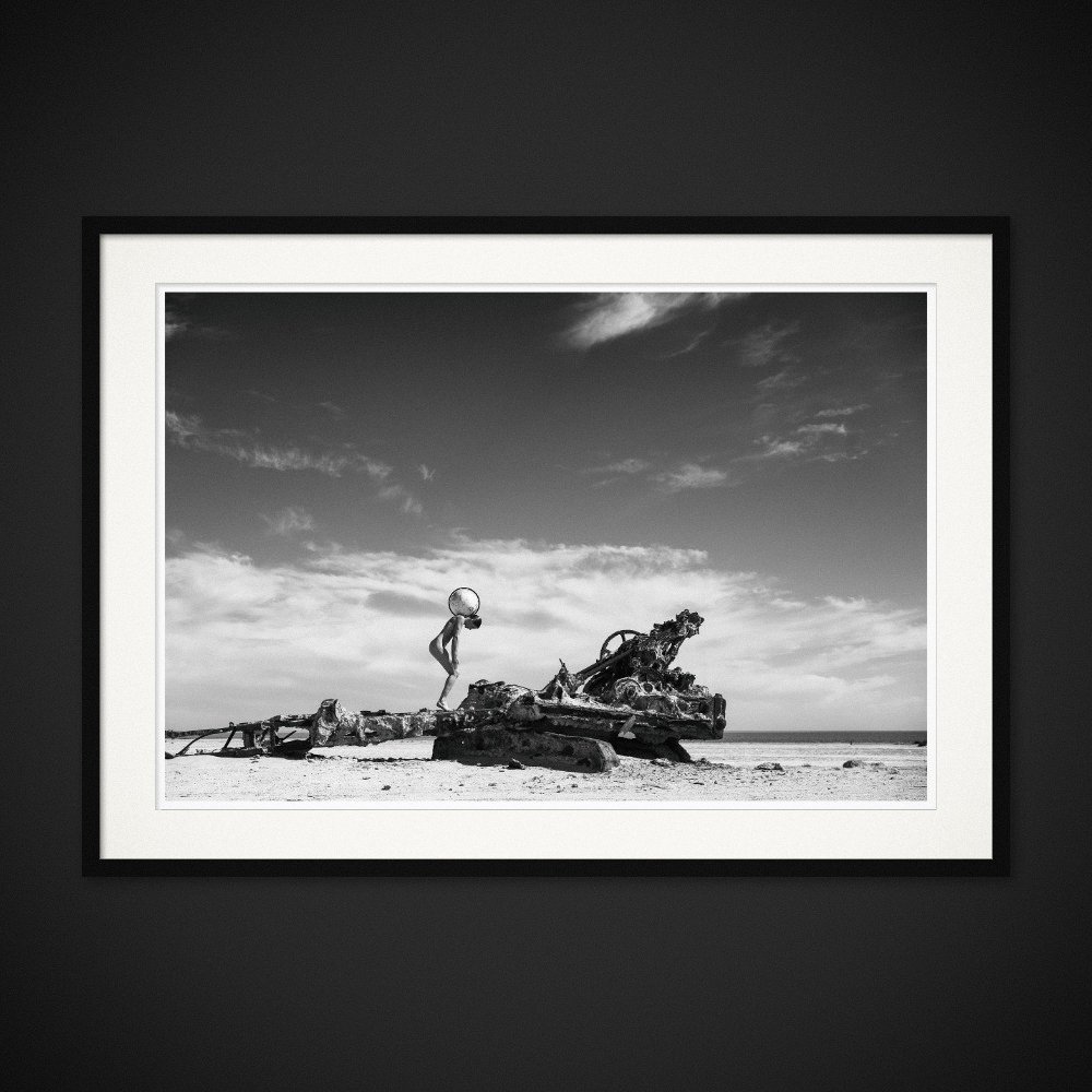 Global Pressure — A figure bends beneath a globe beside the remains of machinery. Framed edition by Albert Pocej.