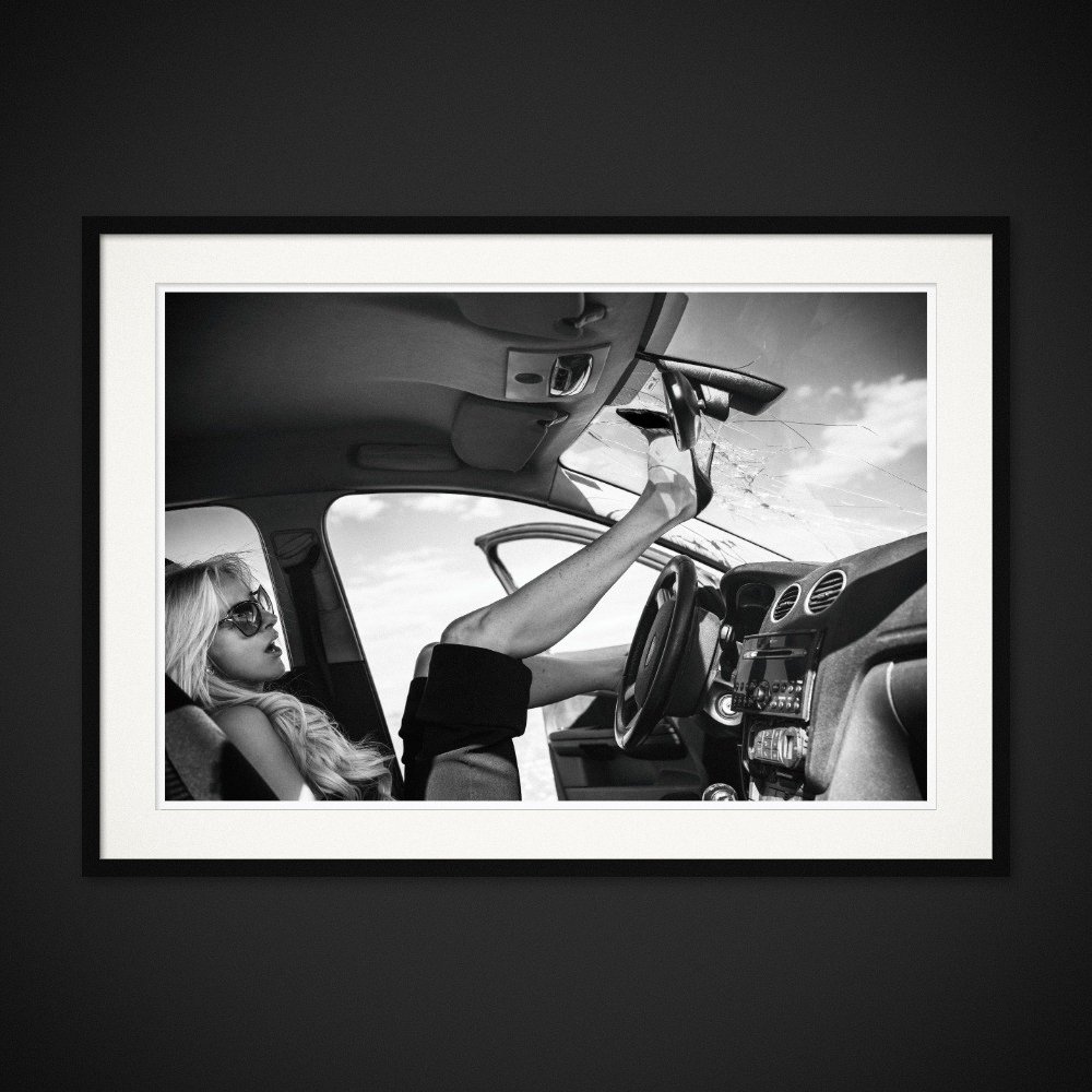 Louboutin Revenge — A high heel reaches the roof of a car from the passenger seat. Framed edition by Albert Pocej.