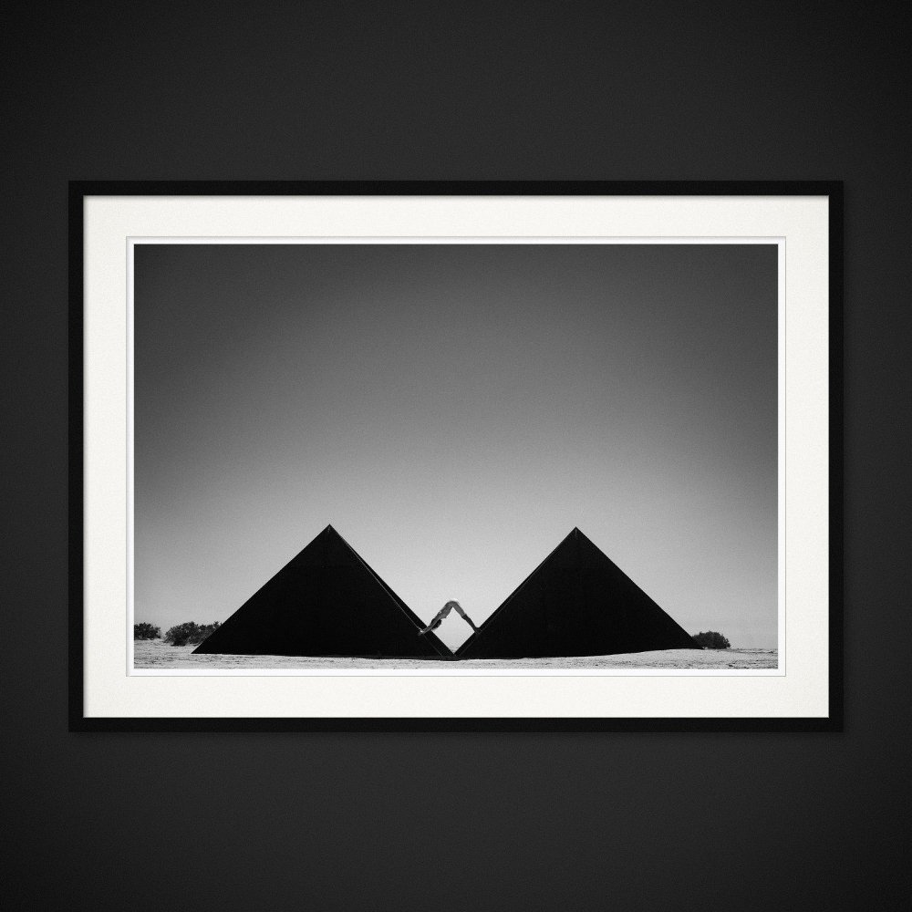 Mind The Gap — A body completes the geometry between two dark triangular structures. Framed edition by Albert Pocej.