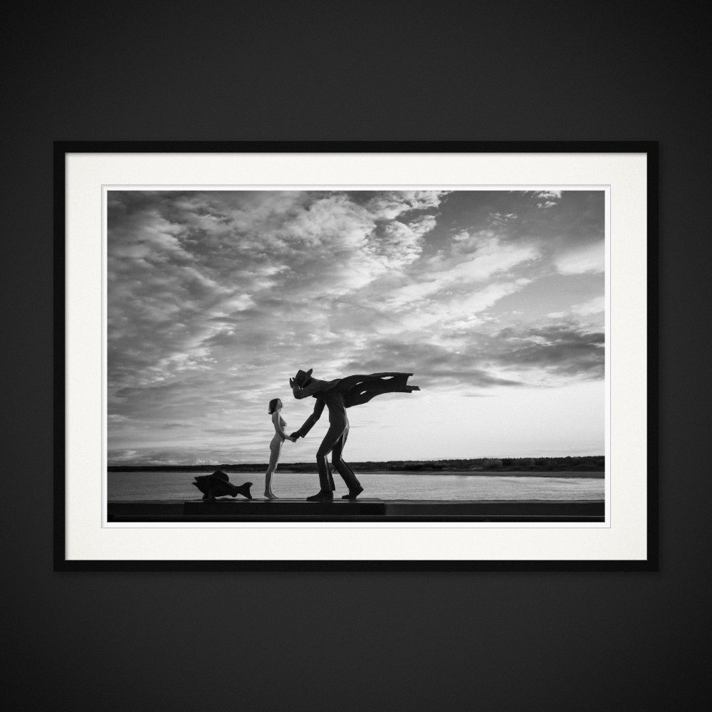 Monumental Love — A human gesture meets a much larger sculptural figure by the sea. Framed edition by Albert Pocej.