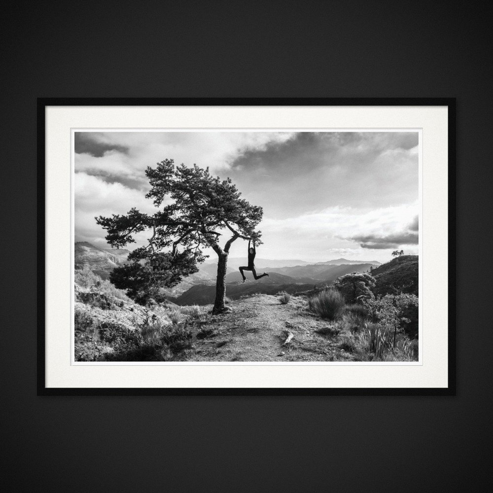 One Kilometre Of Solitude — A figure hangs from a lone tree above the mountain landscape. Framed edition by Albert Pocej.