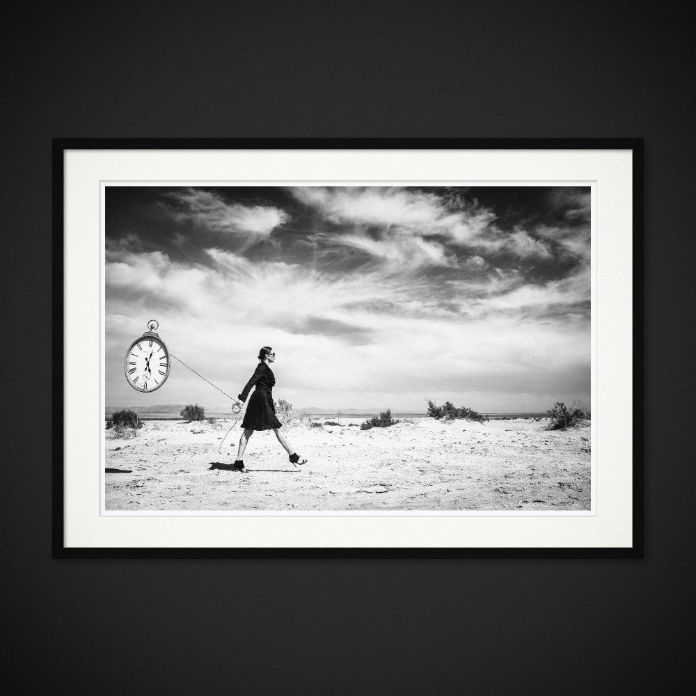 Temporal Baggage — An oversized clock follows a figure across the dry landscape. Framed edition by Albert Pocej.